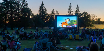 A large group of people are sitting in a field, watching a movie on a big screen.

AI generated content