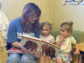 A woman reads a book to two children, one on her lap and another on a chair.

AI generated content
