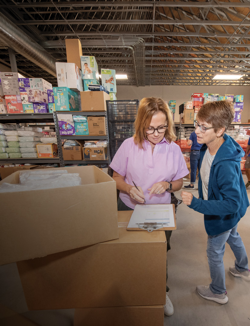 A woman and a man are standing in a warehouse, surrounded by boxes. The woman is wearing a pink shirt and glasses, while the man is wearing a blue shirt. They appear to be engaged in a conversation or task.

AI generated content