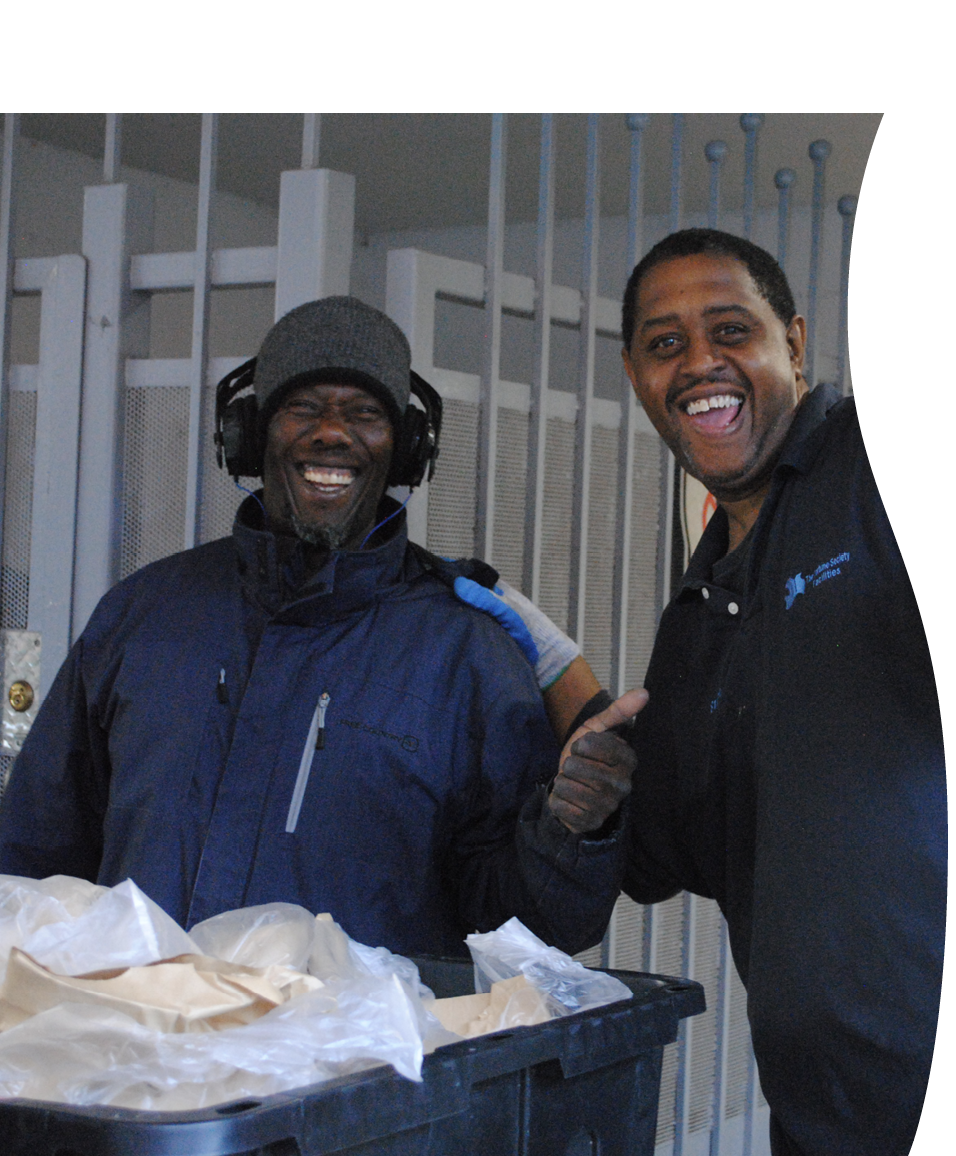 Two men wearing dark jackets laugh and give thumbs-ups to the camera.