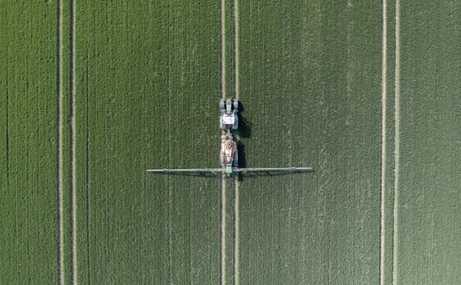 A Tractor Spraying Controversial Glyphosate Herbicide onto Farmland Aerial View.