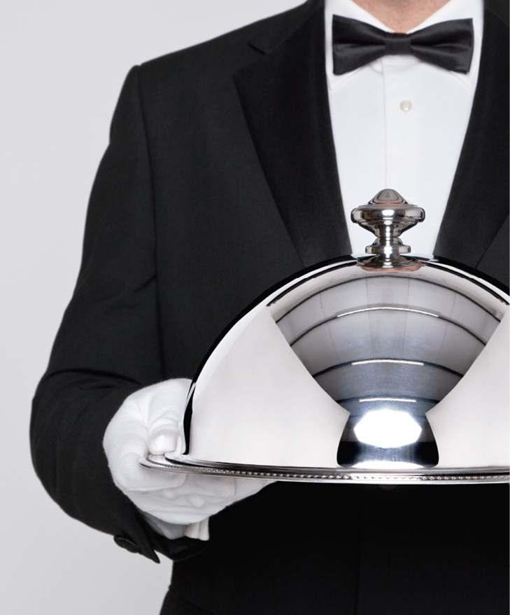 Waiter serving a meal under a silver cloche or dome.