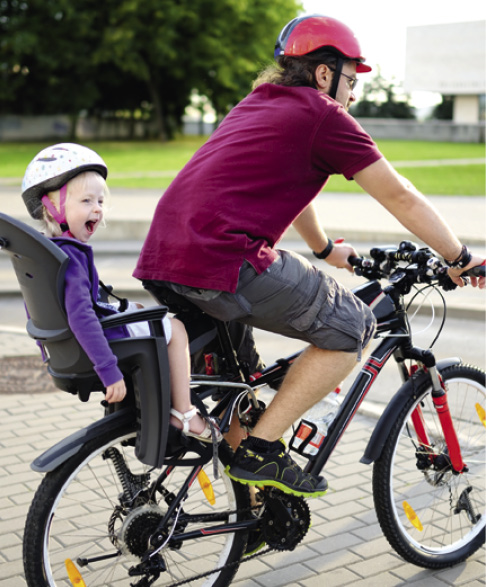 Happy father and his little toddler daughter riding a bike together in a city on summer day.