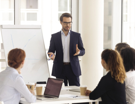 Male business coach speaker in suit give flipchart presentation, speaker presenter consulting training persuading employees client group, mentor leader explain graph strategy at team meeting workshop.